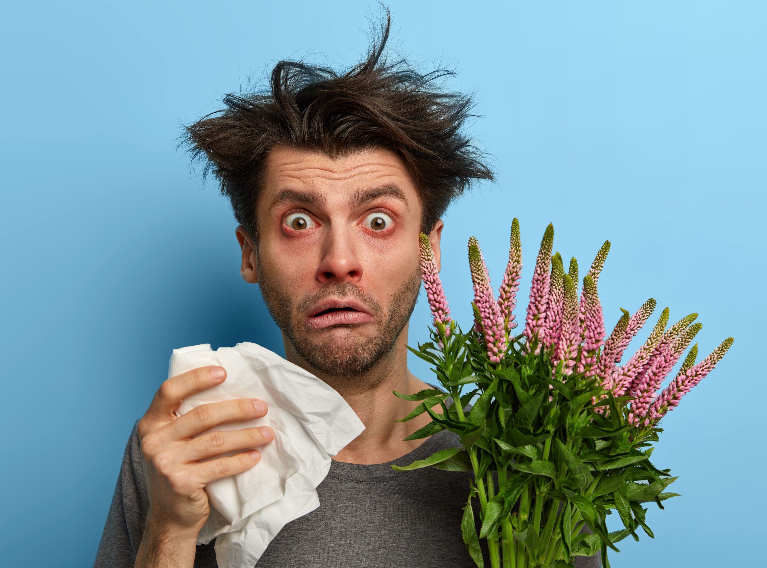 A man holding flowers and a tissue suffering from hayfever